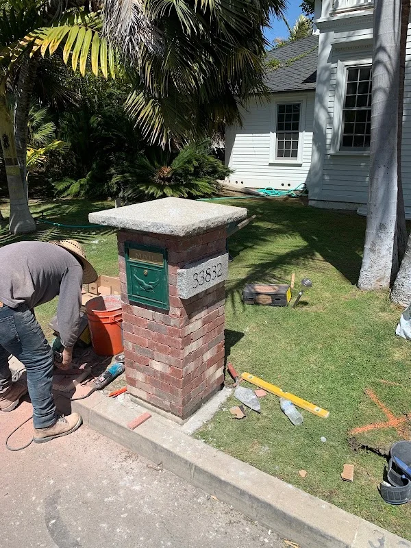 Brick mailbox post with concrete cap and green mailbox fixture during installation