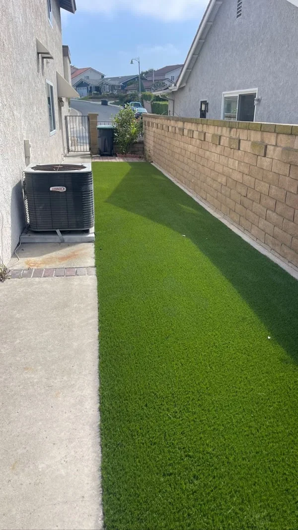 Artificial turf lawn with tan brick retaining wall in residential side yard
