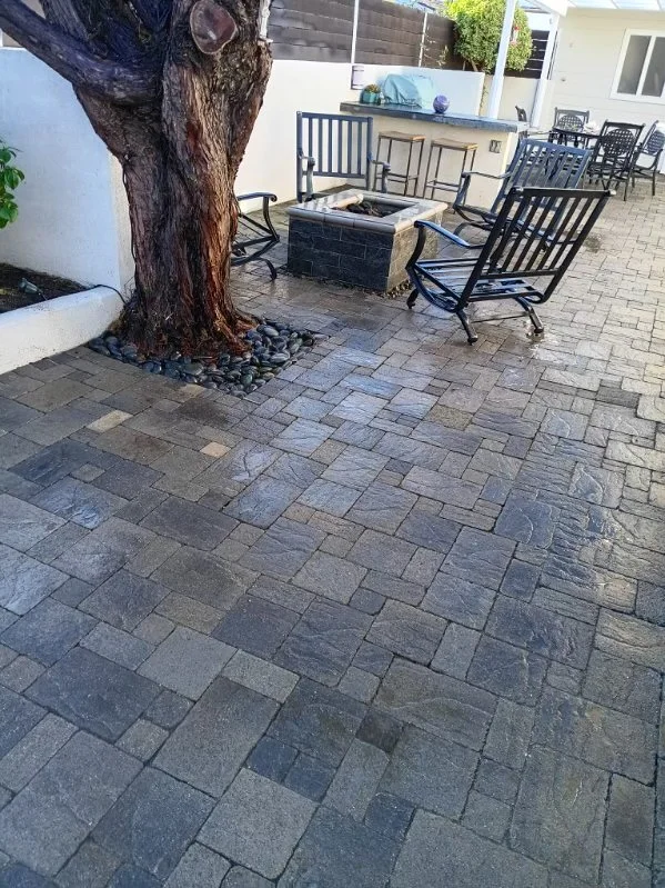 Gray and charcoal paver patio with central fire pit, mature tree, and black outdoor furniture