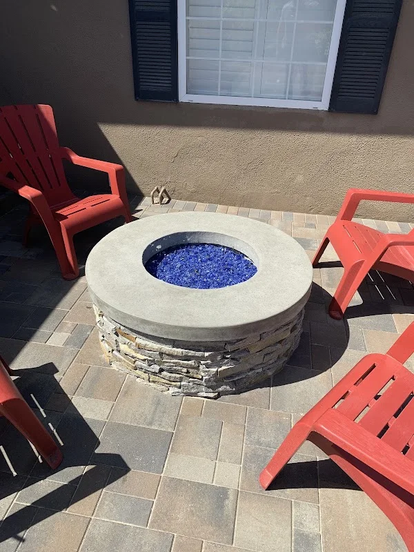 Circular concrete fire pit with blue glass media, stacked stone base, and surrounding paver patio
