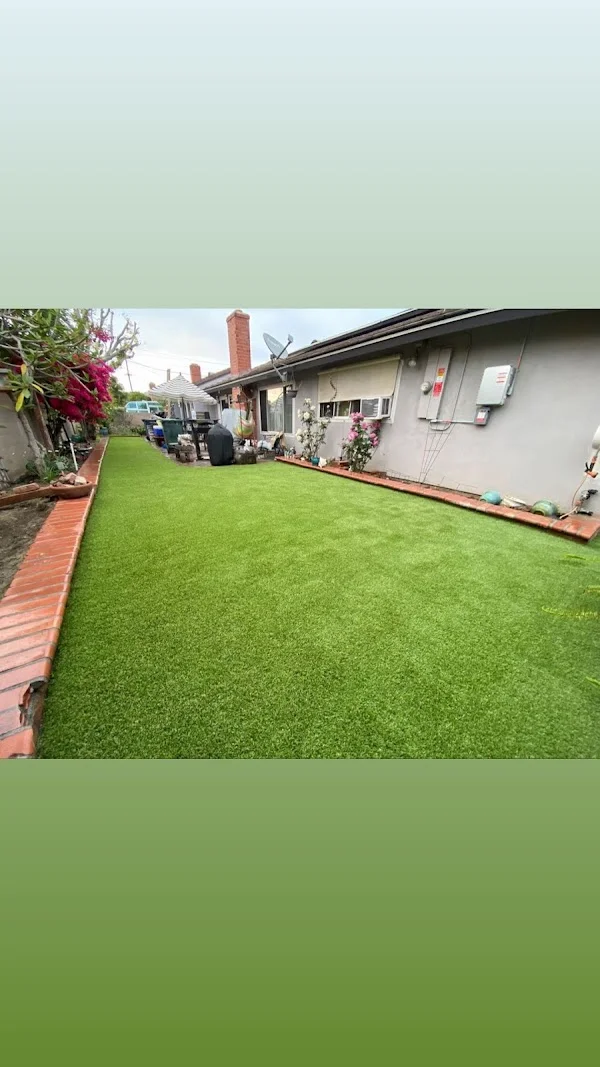 Artificial turf installation in residential backyard with brick edging and house backdrop