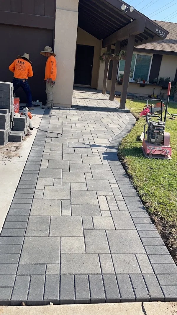 Gray concrete paver patio in running bond pattern with compaction equipment and installation crew