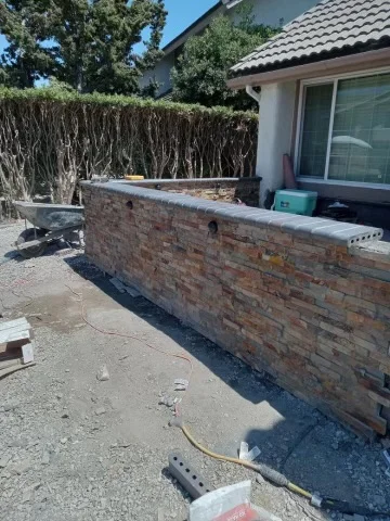 Newly constructed red brick retaining wall with concrete cap and drainage base