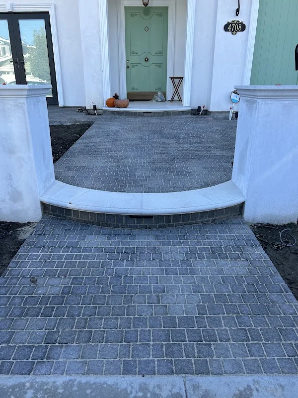 Curved gray brick paver walkway with concrete border leading to front entrance