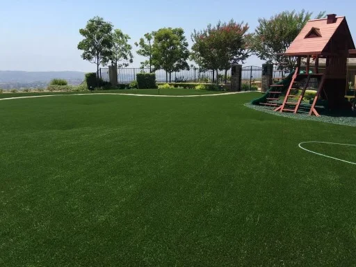 Synthetic turf lawn with mature trees, white fence, and play structure installation