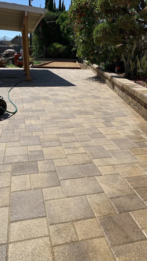 Geometric permeable paver patio with neutral-toned pavers in running bond pattern, concrete retaining wall, and wooden pergola
