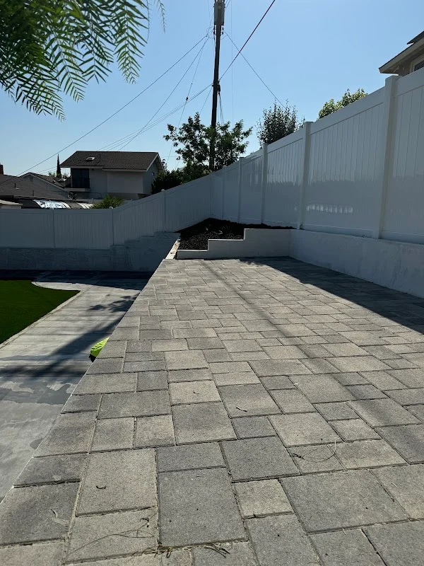 Gray paver patio in herringbone pattern with white vinyl privacy fence and landscaping