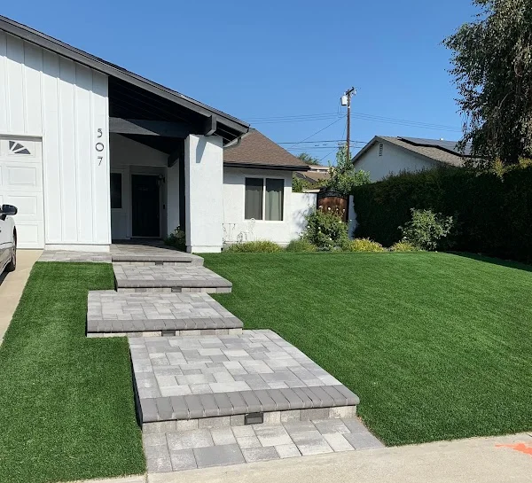 Gray concrete paver walkway with sod lawn installation leading to modern home entrance