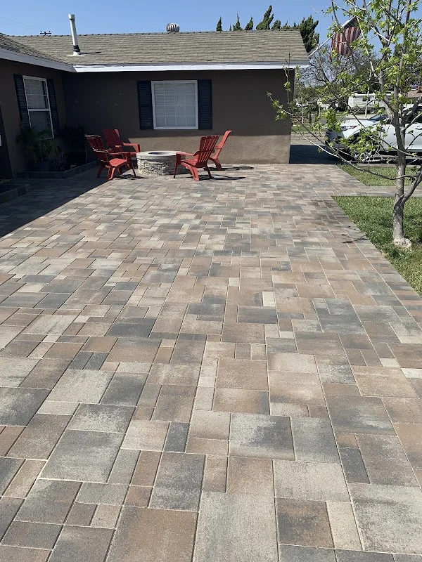 Newly installed paver patio with mixed-width running bond pattern in neutral tones, two red Adirondack chairs, and mature landscaping
